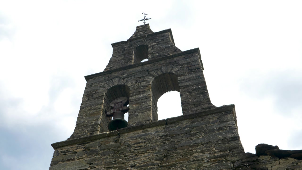 Vista dal basso dello storico campanile in pietra della Chiesa di Santoalla do Monte in Galizia, Spagna, che evidenzia la sua architettura rurale e segnata dal tempo contro il cielo