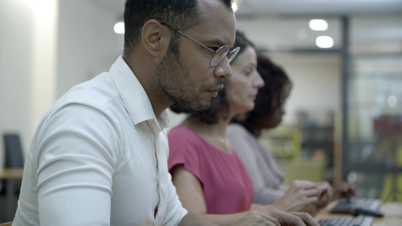 Row of people sitting at table and using computers