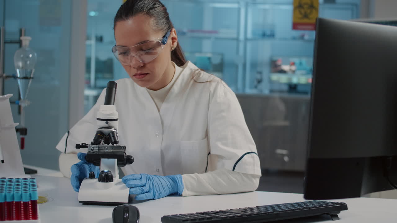 Specialist with safety goggles using microscope in laboratory