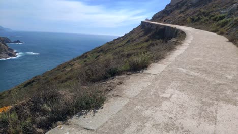 gente subiendo por el camino de la montaña con mirador en la cumbre y la isla en el fondo del mar, día soleado, disparando viajando hacia adelante rodando hacia la izquierda, isla cíes, galicia, españa