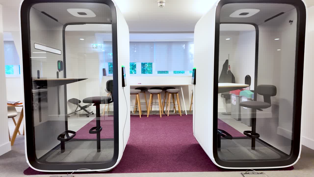 Minimalist soundproof office pods providing a quiet and private workspace for employees needing concentration in a modern coworking space. Pan right