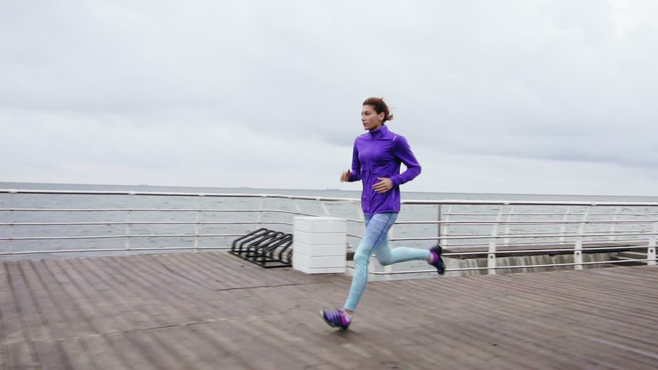 Young athletic woman running outdoors in slow motion on promenade near ocean enjoying early morning run