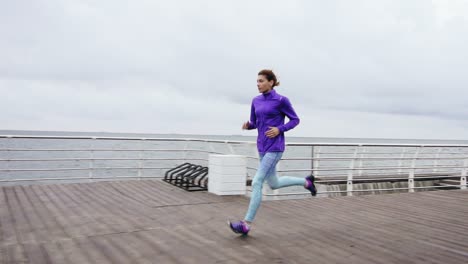 Young-athletic-woman-running-outdoors-in-slow-motion-on-promenade-near-ocean-enjoying-early-morning-run