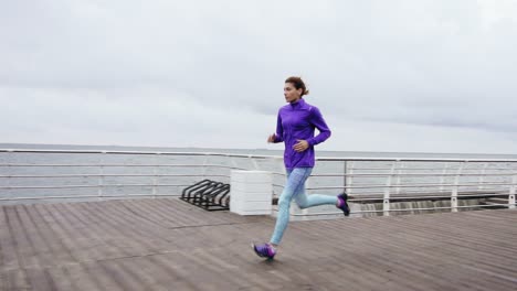 Joven-Atlética-Corriendo-Al-Aire-Libre-En-Cámara-Lenta-En-El-Paseo-Marítimo-Cerca-Del-Océano-Disfrutando-De-Correr-Temprano-En-La-Mañana