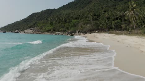 waves breaking on beautiful white sand beach in koh phangan, low aerial