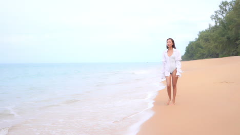 a pretty young woman in a one-piece bathing suit walks up the beach toward the camera