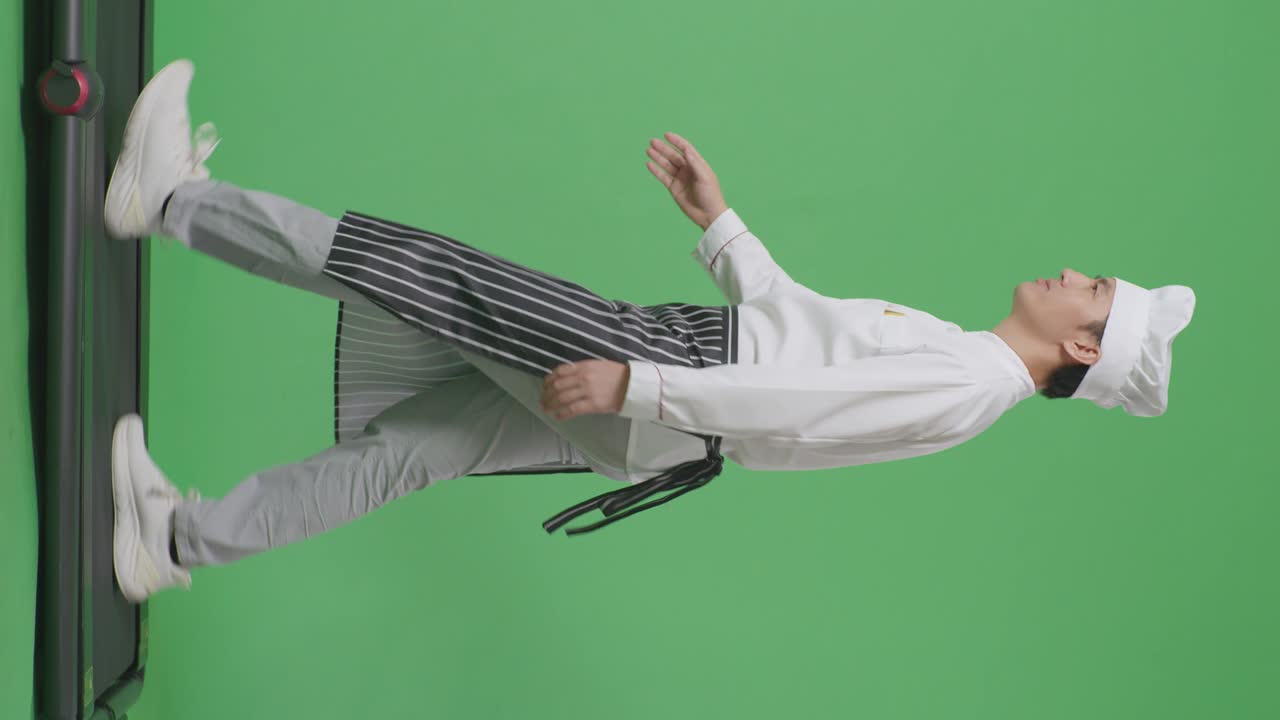 으로 바라보는 시체로 가득 찬 아시아 남성 요리사는 트레드밀을 고 녹색 화면 배경 스튜디오에서 손을 흔들고 있습니다.