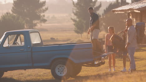 Gruppe-Von-Freunden,-Die-Auf-Dem-Roadtrip-Zu-Einer-Hütte-Auf-Dem-Land-Rucksäcke-In-Einen-Pick-up-Truck-Laden