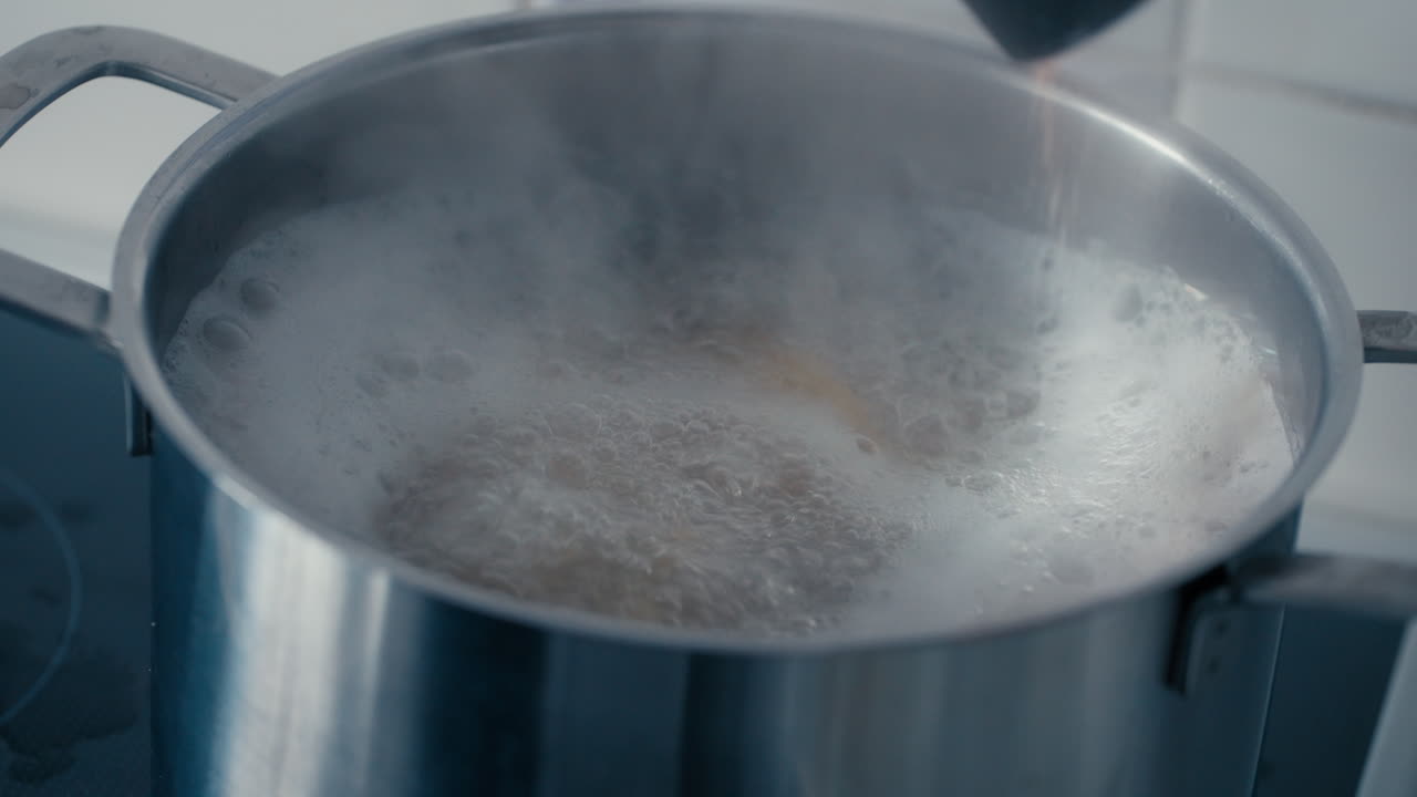 Close up of cooking Pasta Tagliatelle in boiling water in a big steel Pot on the stove and adding Salt to water in the kitchen during a day in slow motion