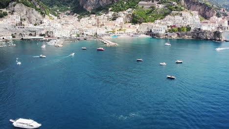 Drohne-Fliegt-über-Das-Meer-In-Richtung-Eines-Küstendorfes,-Beginnend-Mit-Der-Kamera-Nach-Unten-Und-Nach-Oben-Geneigt-An-Der-Amalfiküste-In-Italien-4k