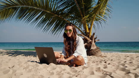 digital nomad woman working on laptop at a tropical beach