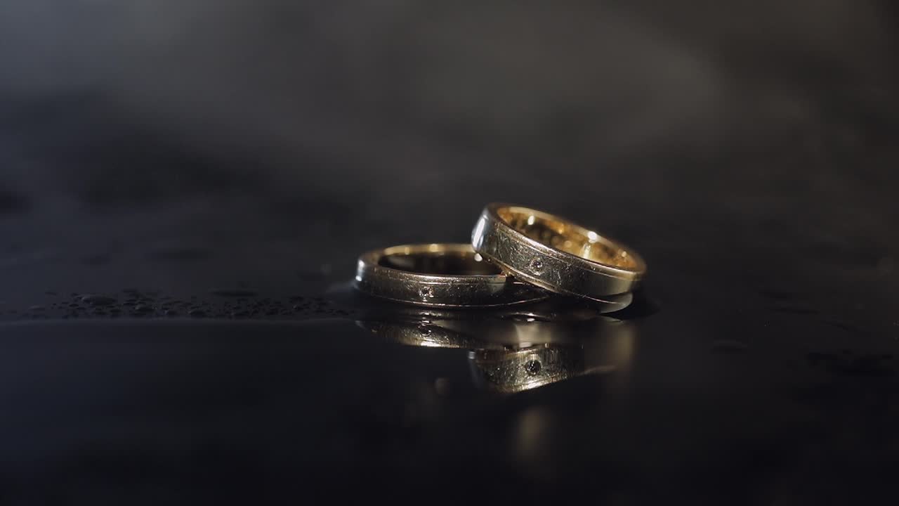 Wedding rings on dark water surface shining with light. Close up macro