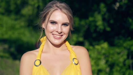 cu portrait young beautiful girl in a big yellow evening dress posing against a background of foliage smiling