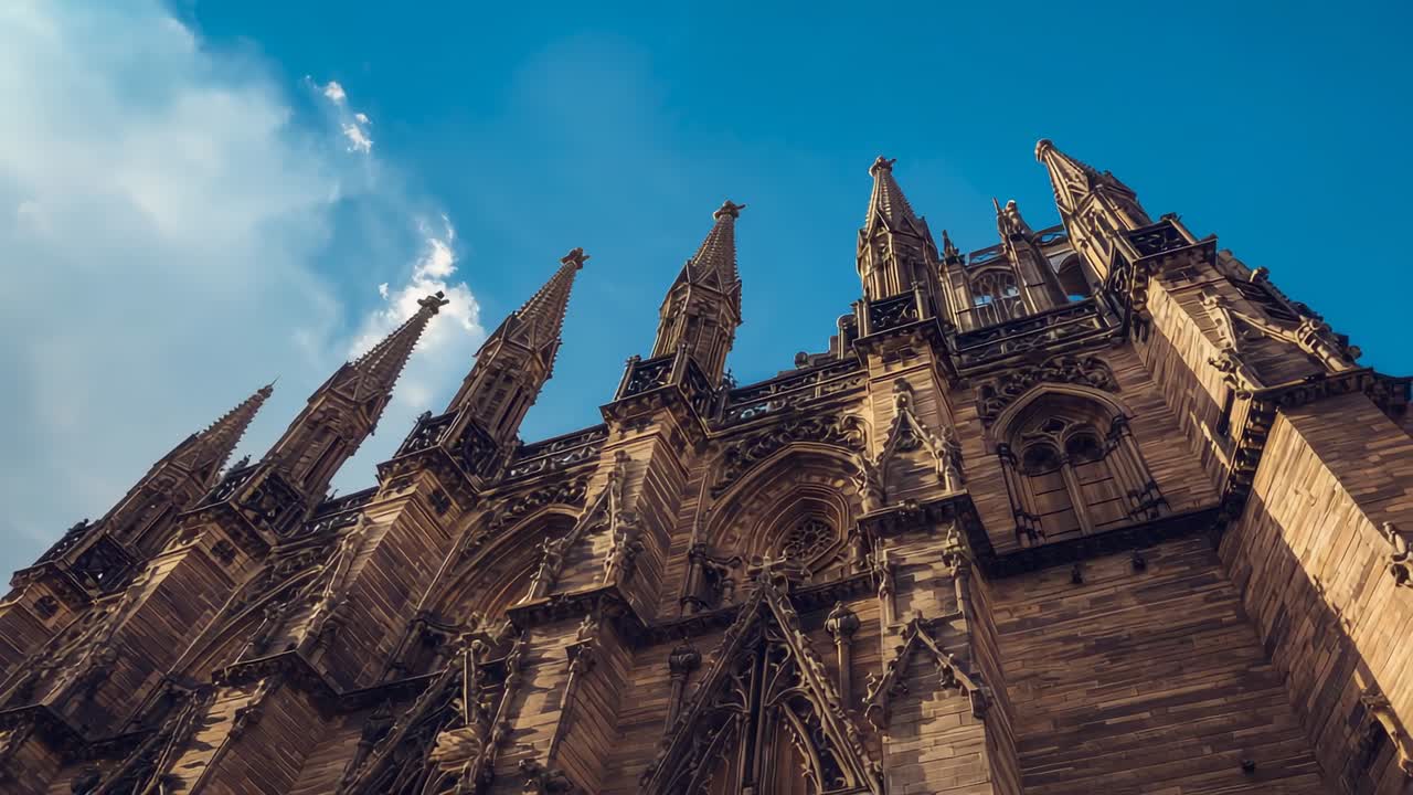 Tilting camera upward from Gothic cathedral facade in plaza, revealing carvings and spires