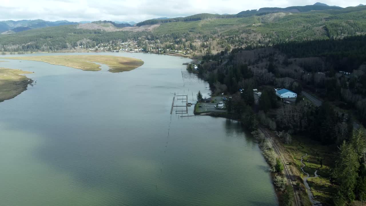 US, Oregon, Garabaldi, Nehalem Bay, 2025-03-18 - Drone view of Nehalem Bay, with old pilings in the river, a boat launch and dock, and an RV park on shore.