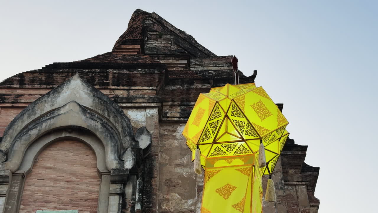Close-up of a yellow lantern spinning in the wind, with the stone top of Watchediluang Varaviharn temple in the background - Thailand