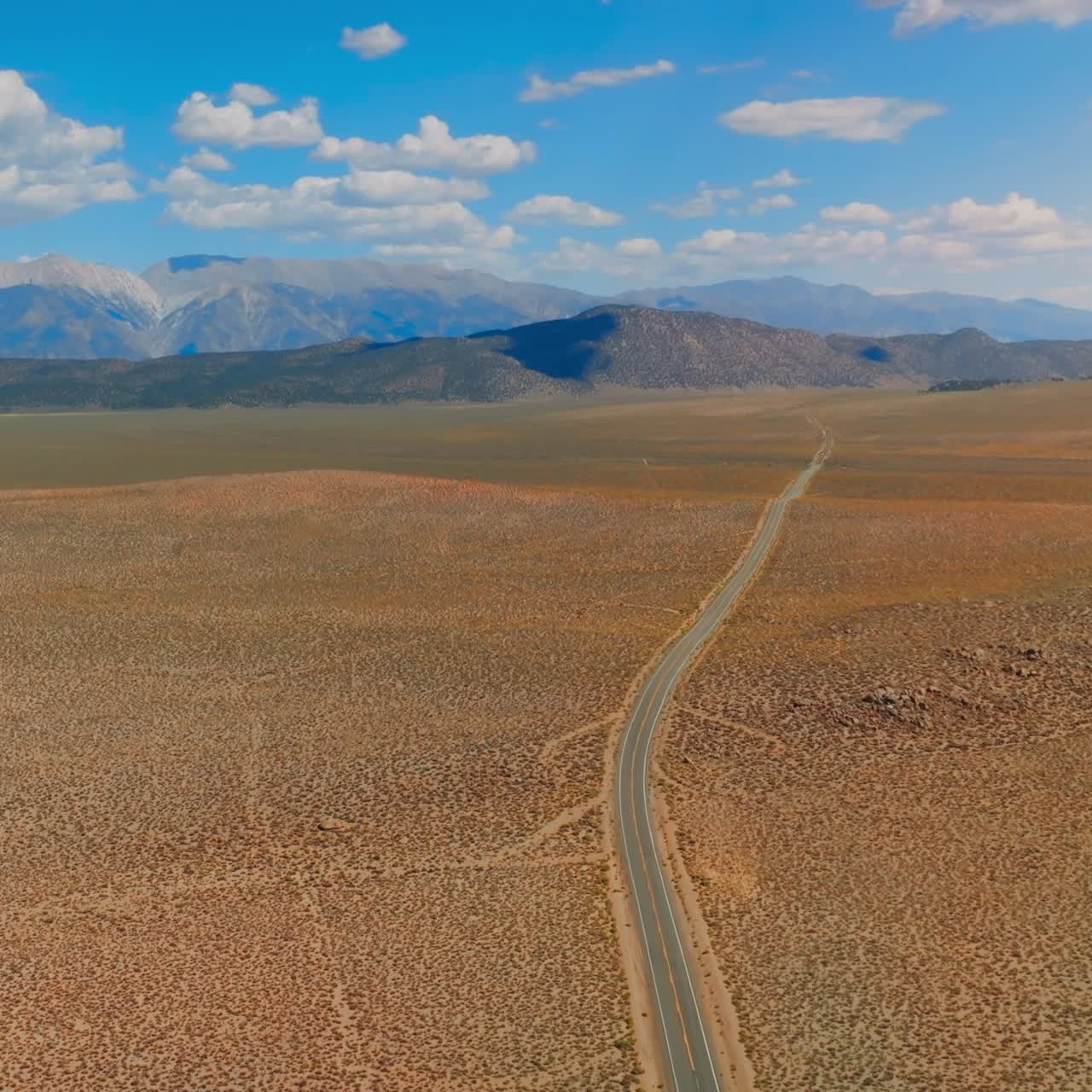 Road passing through the plain deserted landscape of United States. Picturesque mountains of itinerary for California to Nevada at sunny daytime