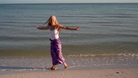 Pretty-mature-woman-wearing-white-top-and-batik-skirt-walking-along-the-shore-at-a-resort-and-smiling-at-camera