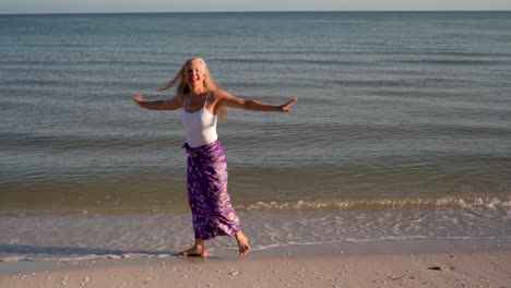 pretty mature woman wearing white top and batik skirt walking along the shore at a resort and smiling at camera