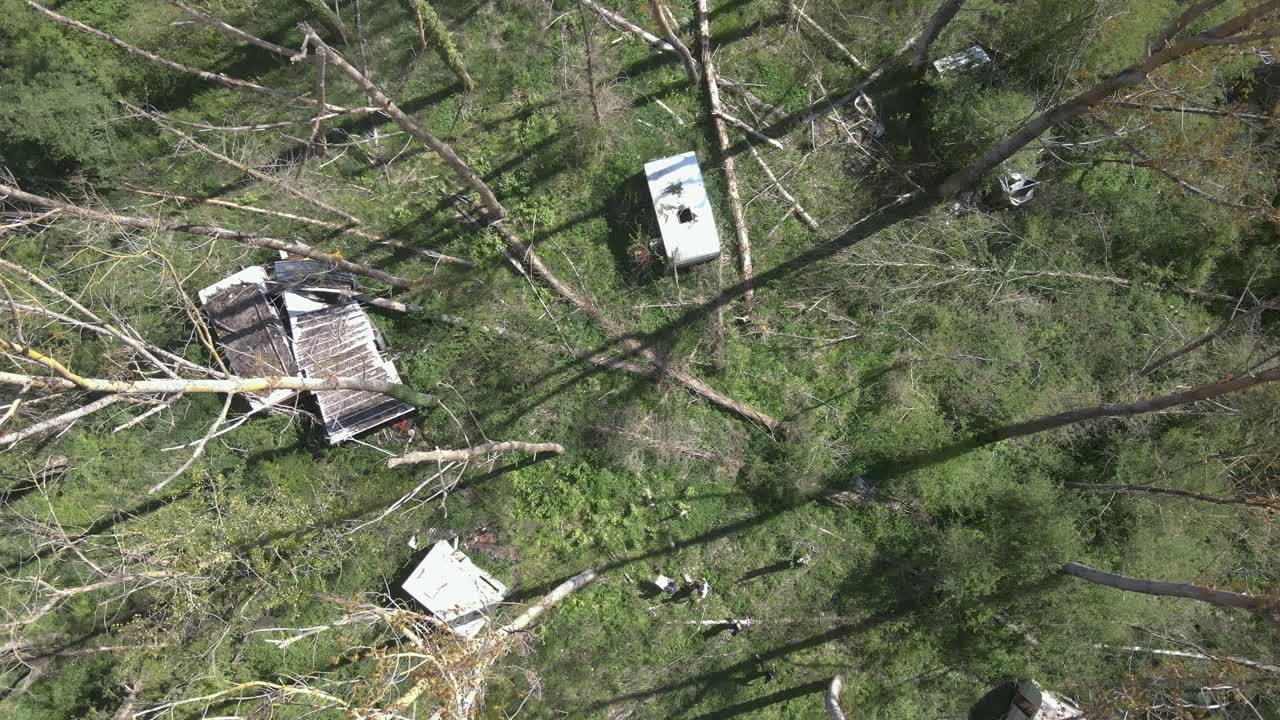 Static drone shot capturing abandoned caravans in a field as people explore