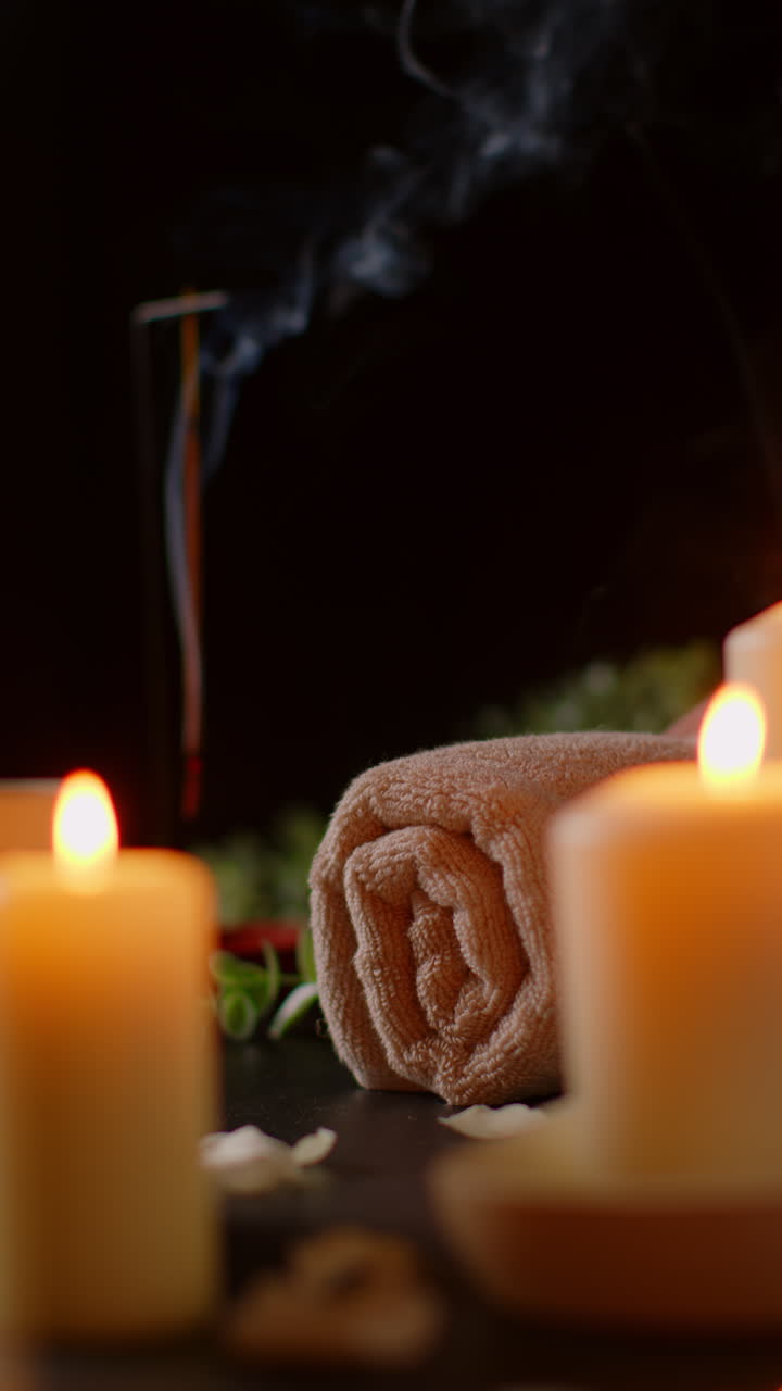 Vertical Video Shot Of Person Putting Down Towel With Lit Candles With Scattered Petals Incense Stick Against Dark Background As Part Of Relaxing Spa Day Decor
