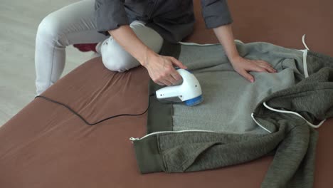 wireless device for cleaning knitted fabrics from lint. the woman is removing the lint from the sweater.