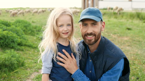 portrait of caucasian young father with cute little daughter and smiling at camera in green field