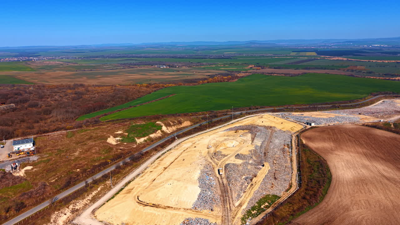 Luftaufnahme einer großen kommunalen Mülldeponie für feste Abfälle. Drohnenaufnahme einer Mülldeponie, umgeben von grünen landwirtschaftlichen Feldern und Hügeln unter klarem blauem Himmel