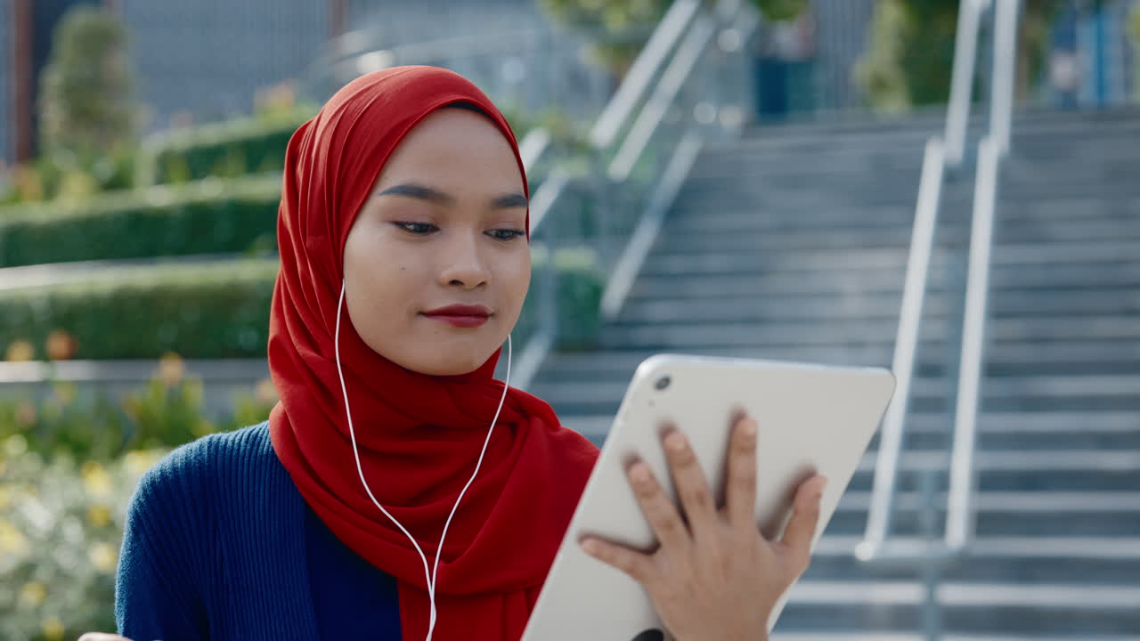 Young Muslim Woman Using Tablet with Earphones Outdoors