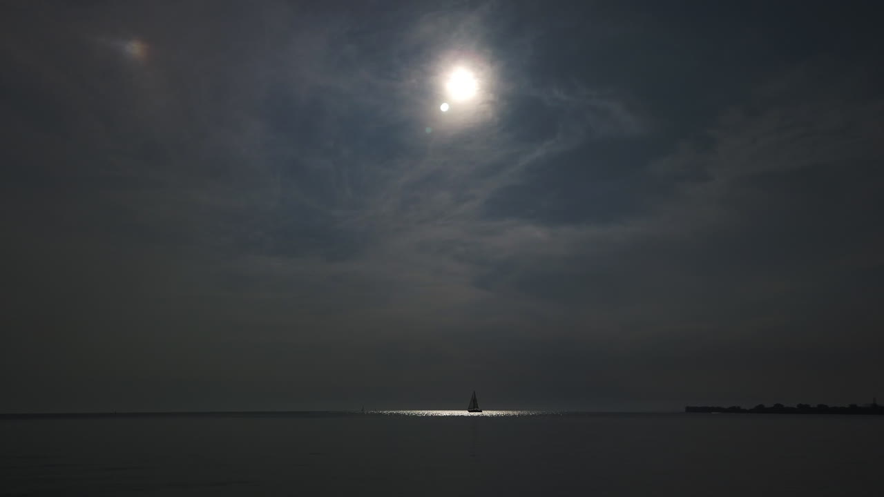 A sailboat in the distance moving slowly through a beam of sunlight on Lake Ontario's waters, wide shot
