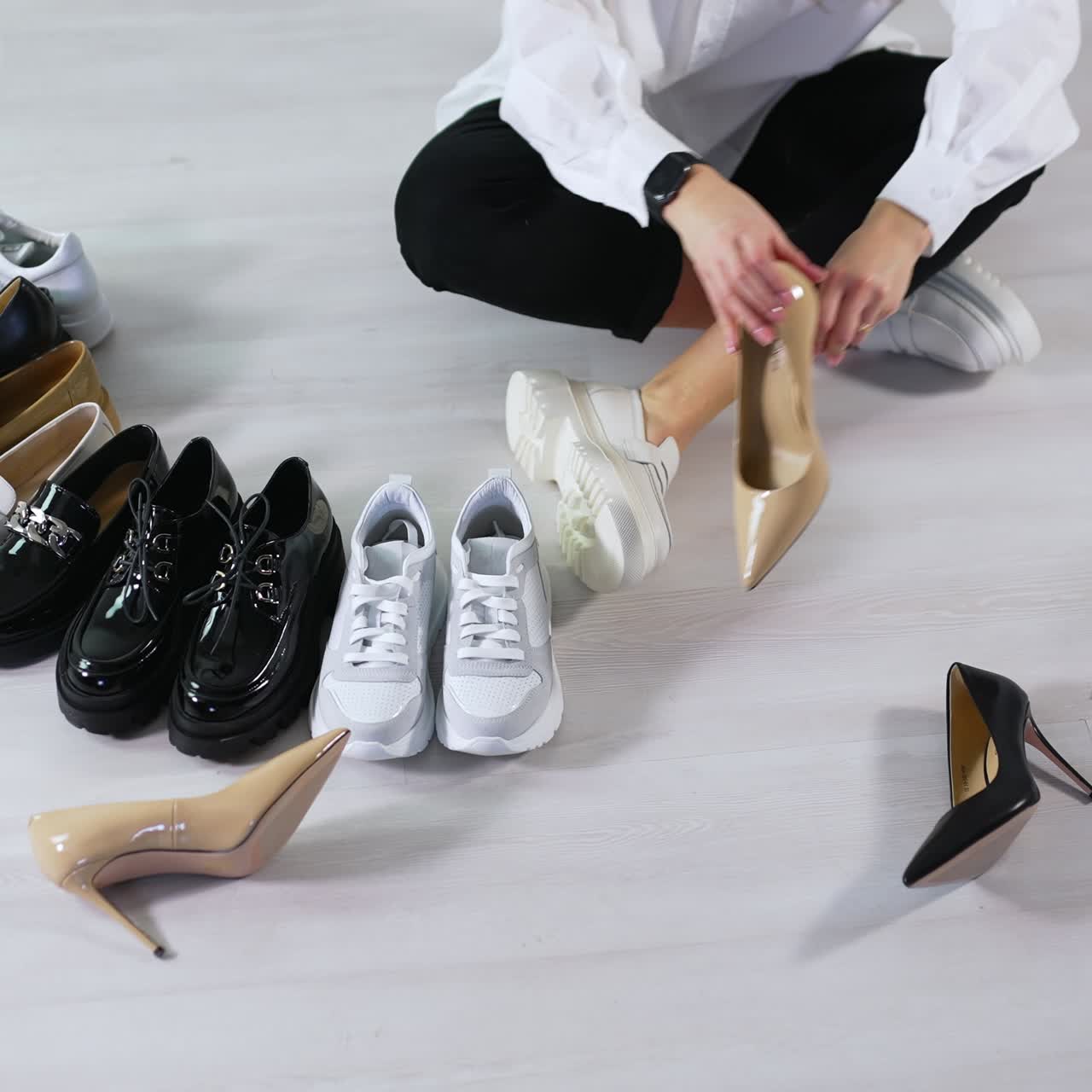 Lady on the floor puts different shoes in pairs in front of hers. Demonstrating the diversity of female footwear. White backdrop