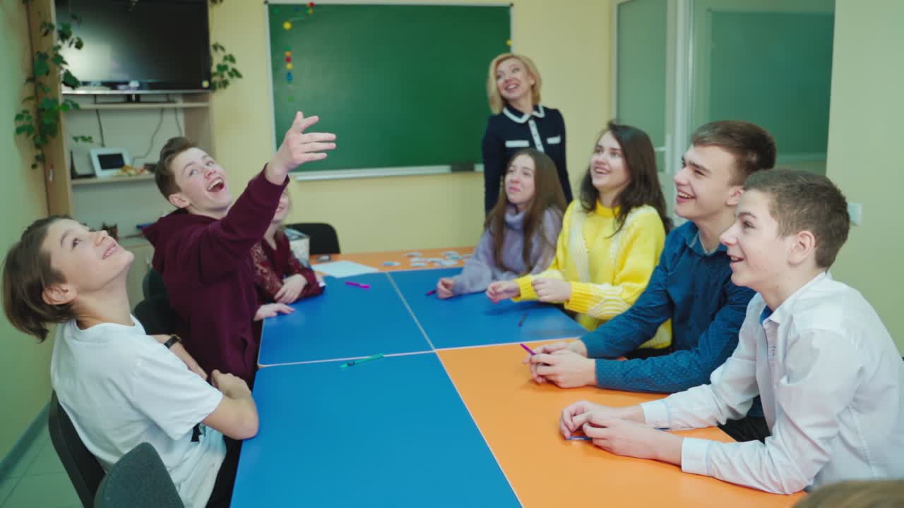 Happy students in the classroom. Pupils having fun together at school. Boy is throws up paper and all children laughing. Slow motion.