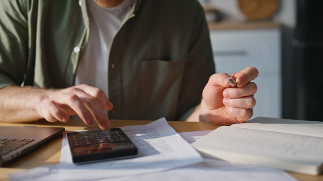Serious man accounting bills working laptop in apartment kitchen closeup
