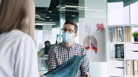 vista trasera de una doctora caucásica sentada en el escritorio explicando la enfermedad pulmonar por coronavirus a un paciente masculino con máscara médica en consulta médica