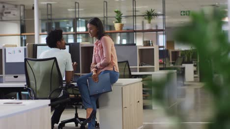 video of diverse businesswoman and businessman using laptop and talking in office