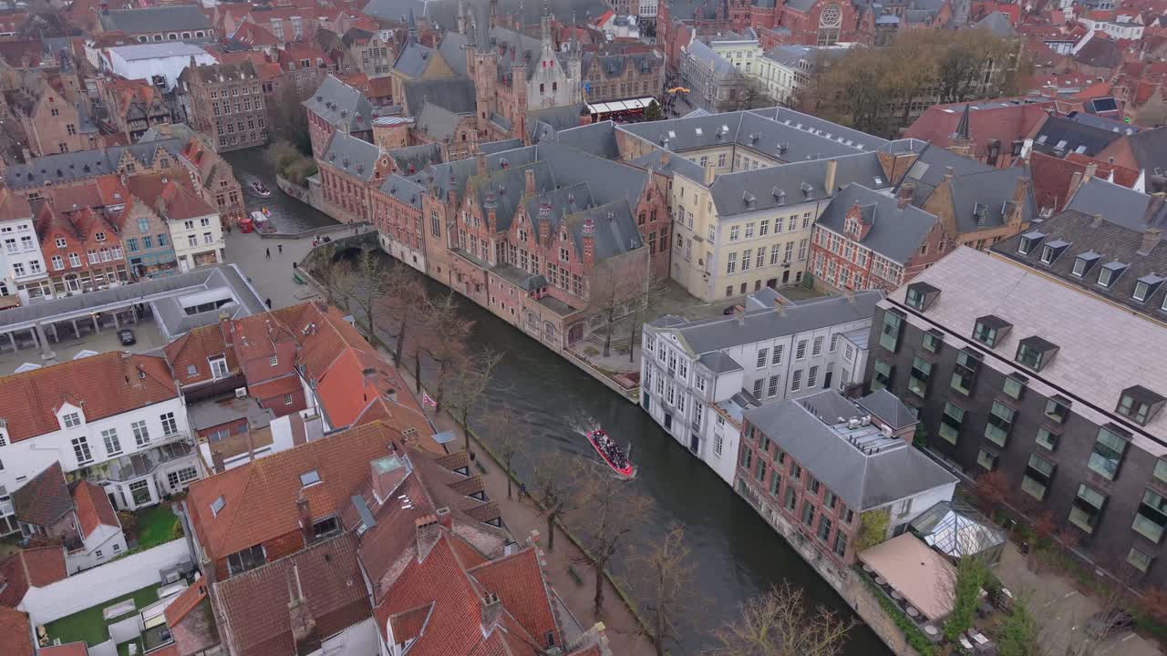 Droneoptagelse af turister på en bådtur, der sejler gennem Brugges historiske kanaler. Smuk middelalderarkitektur og vandaktiviteter i den berømte belgiske by