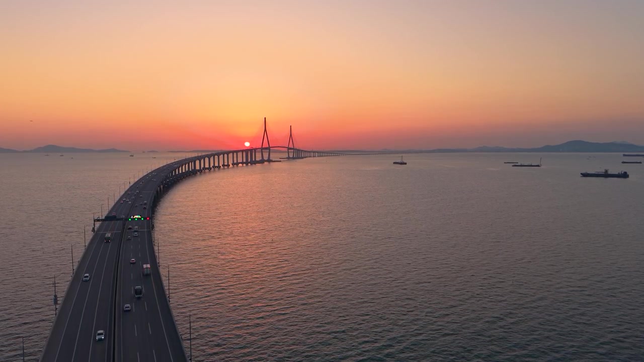 Vista aerea mostra il sole che tramonta direttamente dietro la torre del ponte strallato di Incheon mentre il traffico attraversa il viadotto curvo su un mare calmo