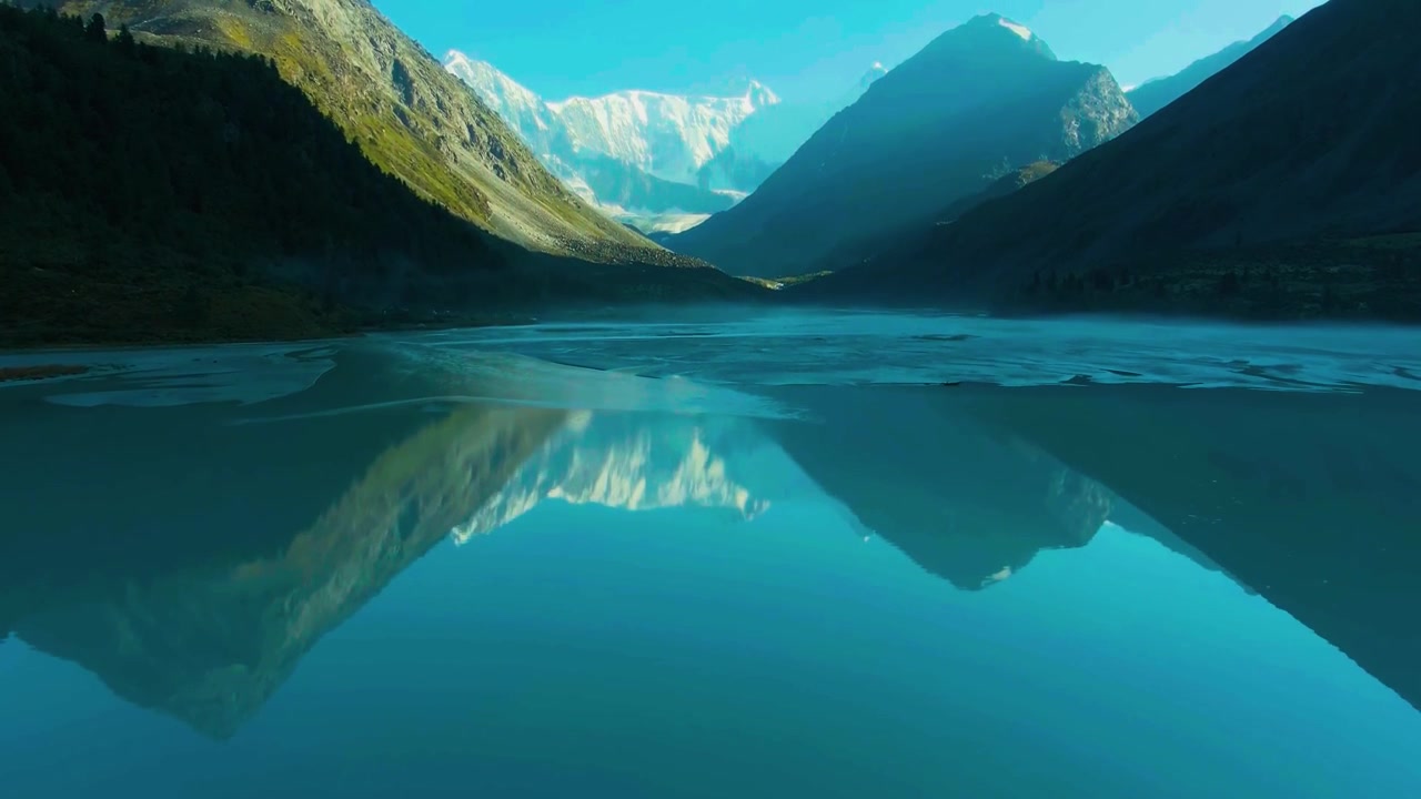 Sunlit peaks tower over a winding river flowing across a remote alpine valley floor.