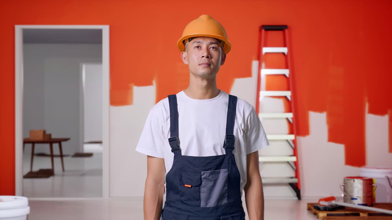 Asian Man Painter Wearing Safety Helmet Standing And Look Around With Painting Wall In Room