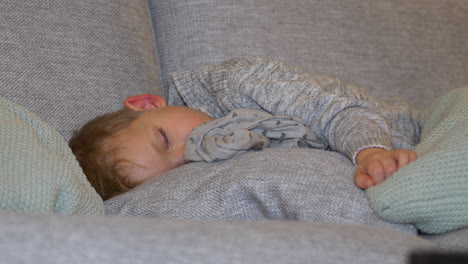 young child sleeps peacefully on grey couch cushions