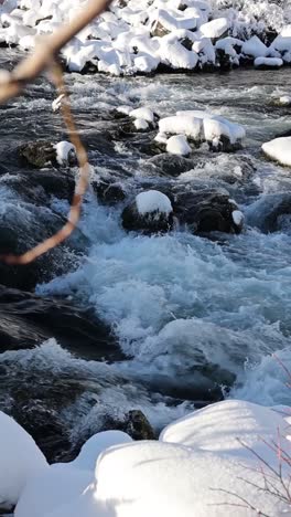 Vertical-slow-motion-dolly-of-snow-covered-rapids-in-a-serene-winter-setting