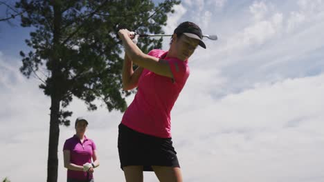 Two-caucasian-women-playing-golf-one-taking-shot-from-bunker