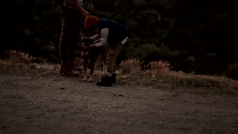 joven padre e hijo excursionistas acariciando al perro en las montañas