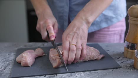 mujer cortando pecho de pollo crudo