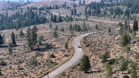 from above: pickup truck travels dusty desert road in forested landscape