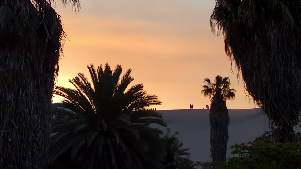 일몰 동안 페루 와카치나 모래 언덕을 걷는 사람들의 실루엣