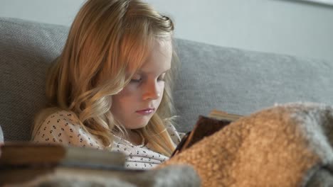 Beautiful-blonde-girl-sitting-on-couch-and-reading-book,-static-view