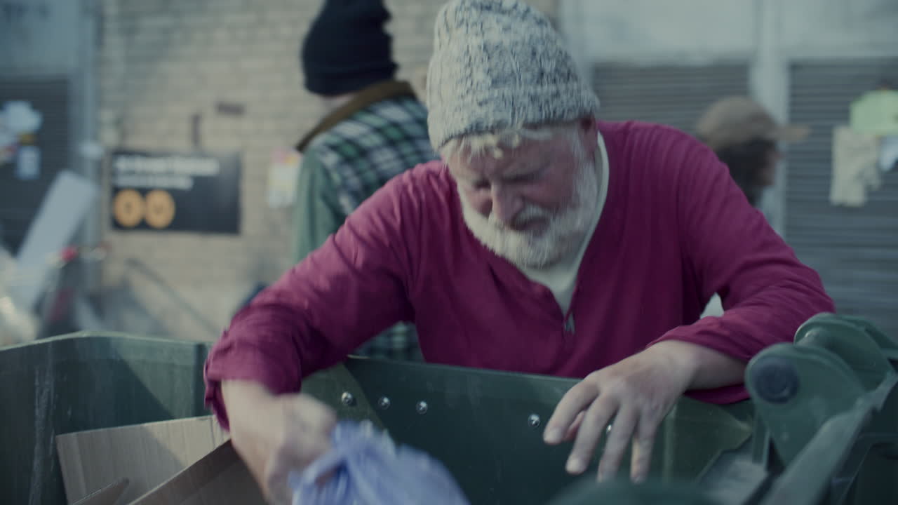 Elderly Homeless Man Searching through Trash Bin on Street