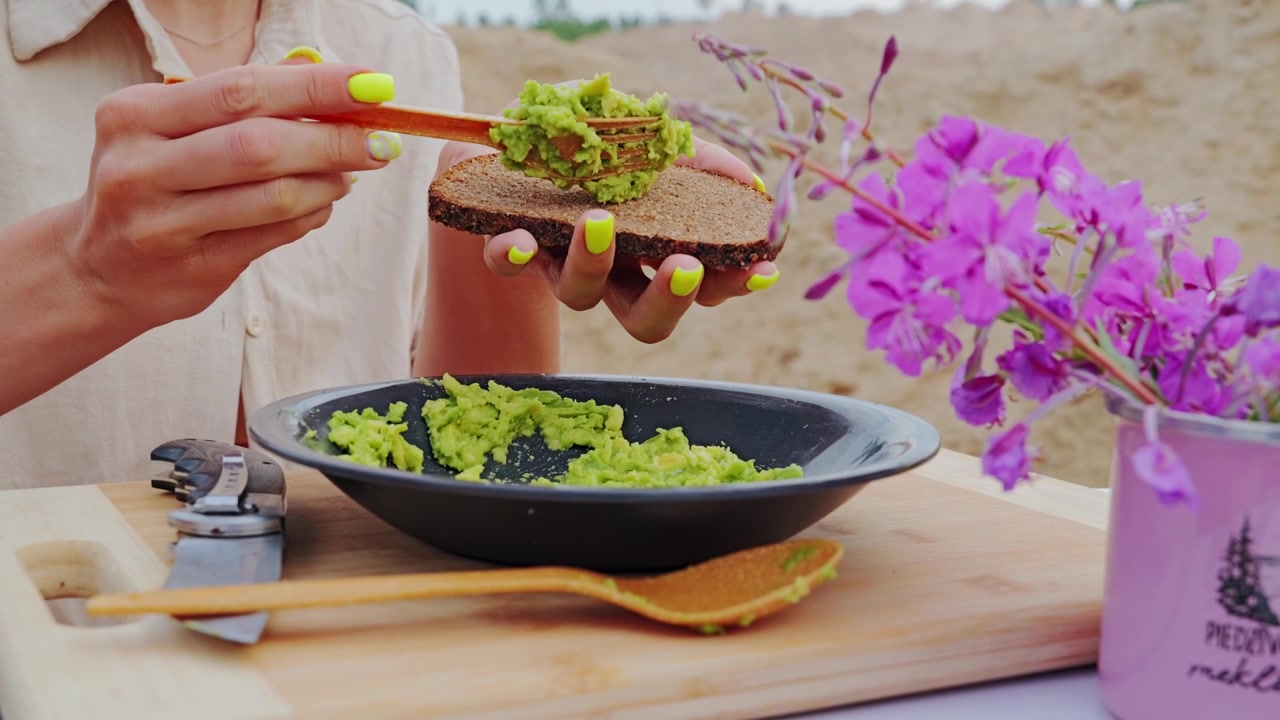 Primo piano di crema di avocado su pane scuro accanto ad accessori da picnic in carta riciclata