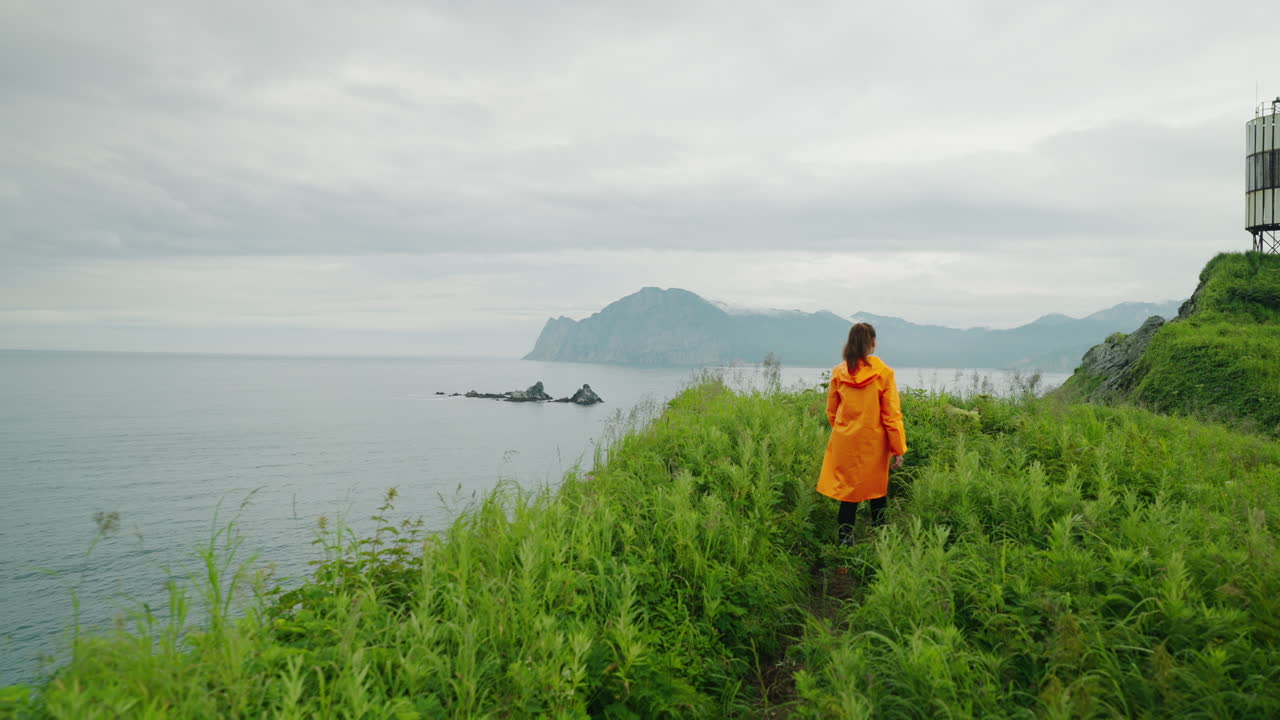 Woman Hiking Along Coastal Cliff in Orange Raincoat